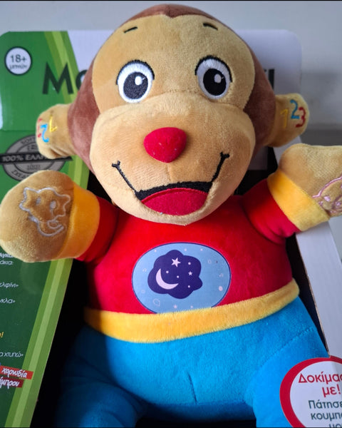 Plush monkey toy with a red shirt and blue pants, in packaging box featuring greek text